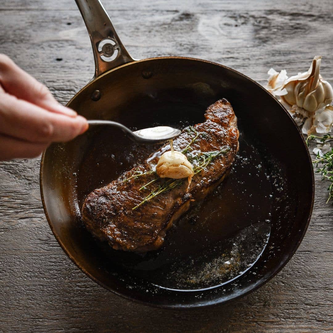 Fried steak with garlic butter being added in a frying pan on a wooden surface