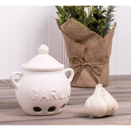 White ceramic garlic keeper with 'Garlic' text, a bulb of garlic, and a potted plant on a wooden surface.