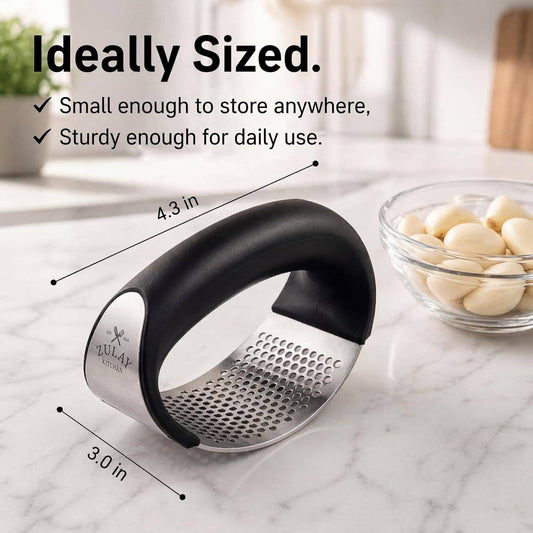 Black and silver garlic press on a marble surface with text indicating its size and features.