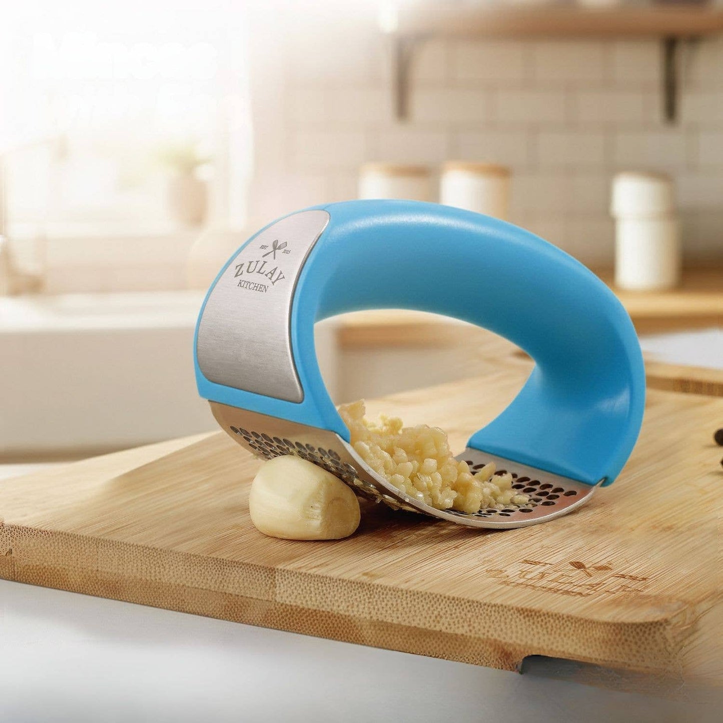Blue kitchen garlic tool on a wooden cutting board with garlic being crushed.
