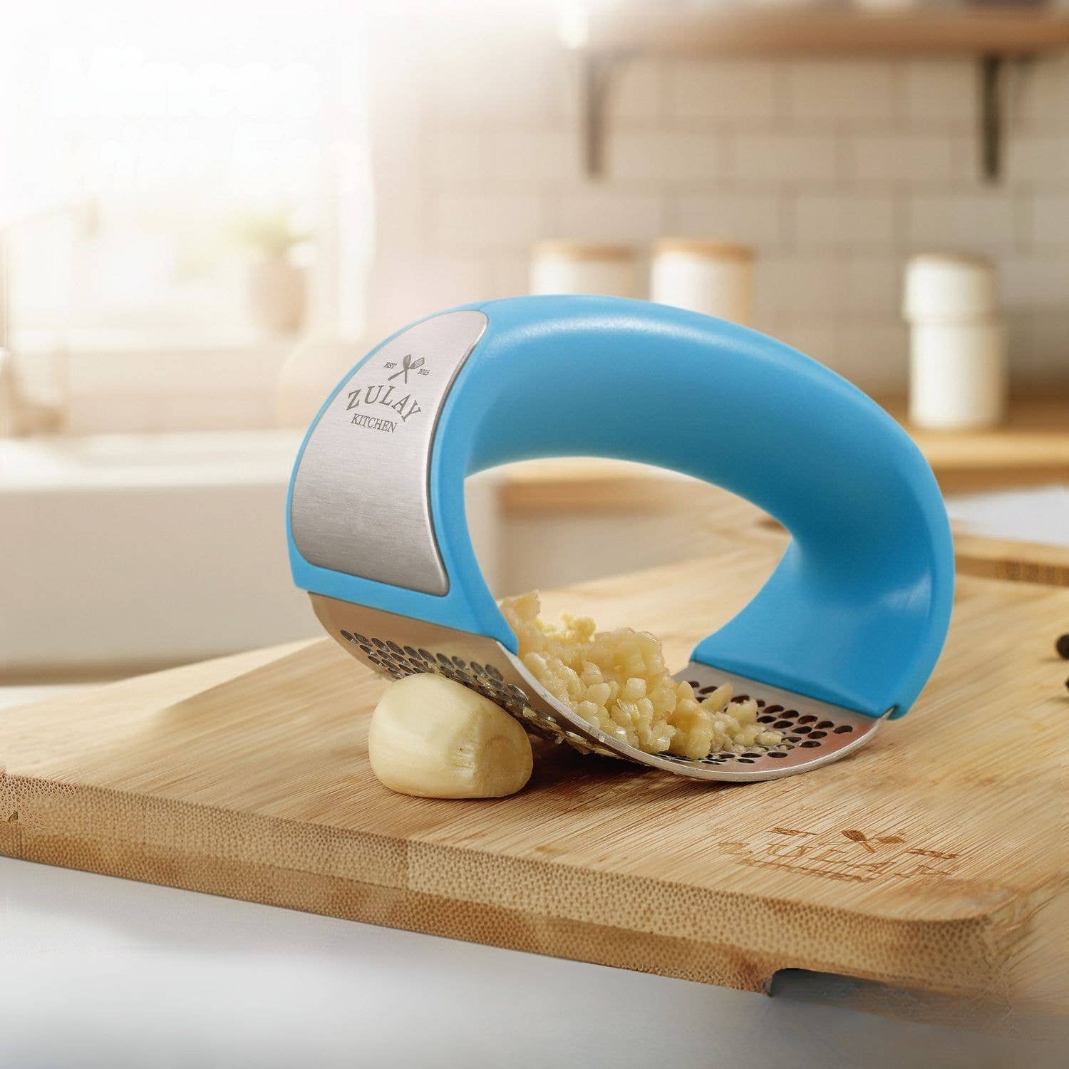 Blue kitchen garlic tool on a wooden cutting board with garlic being crushed.