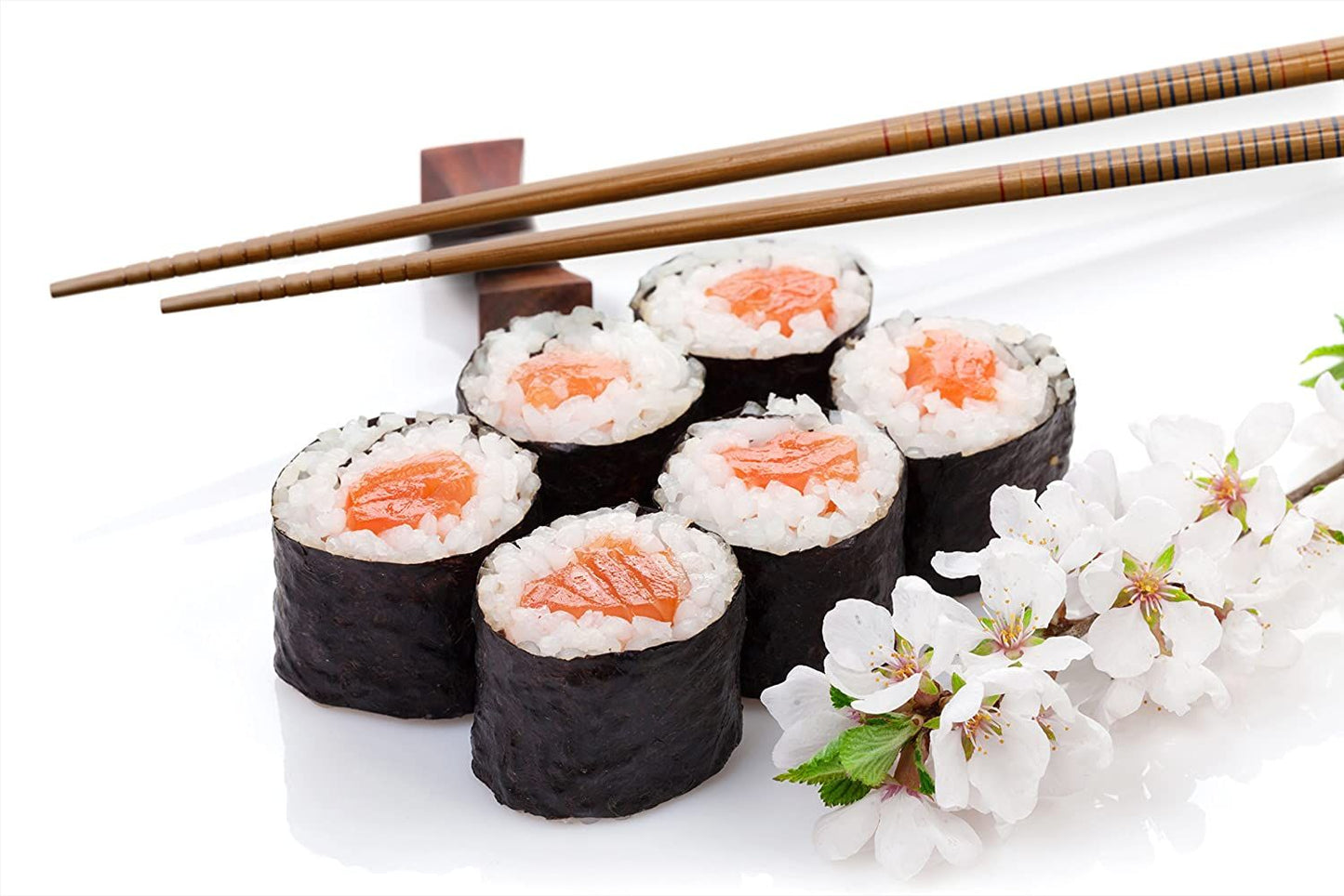 Sushi rolls with salmon on a white surface with cherry blossom flowers and chopsticks.
