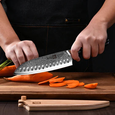 Person using a Klaus Meyer Luxor Santoku knife to slice carrots on a wooden cutting board