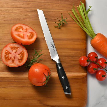 Wooden cutting board with sliced tomatoes, a Klaus Meyer Stahl Serrated Utility  knife, and vegetables on a white background