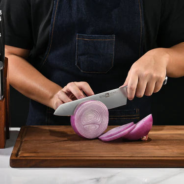 Person cutting red onions on a wooden cutting board with a Klaus Meyer Stahl Chef's  knife.