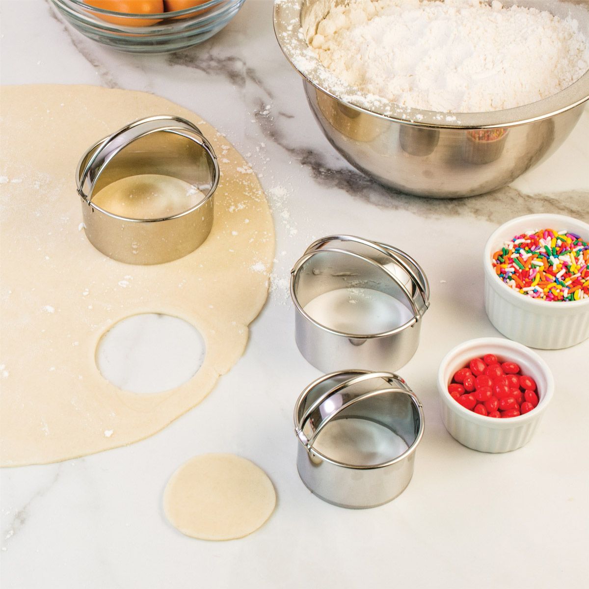 Stainless steel biscuit and cookie cutters on a marble surface with dough and ingredients