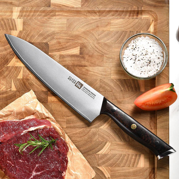 Klaus Meyer Rondure Chef's knife on a wooden cutting board with raw meat, salt, and pepper.