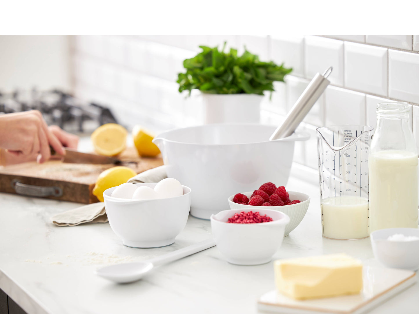 Kitchen counter with Rosti Margrethe bowls of ingredients and a person preparing food.