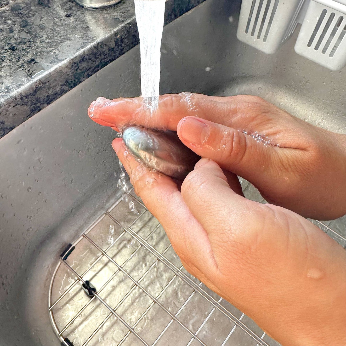 Hand washing using the stainless steel soap bar under running water in a sink.