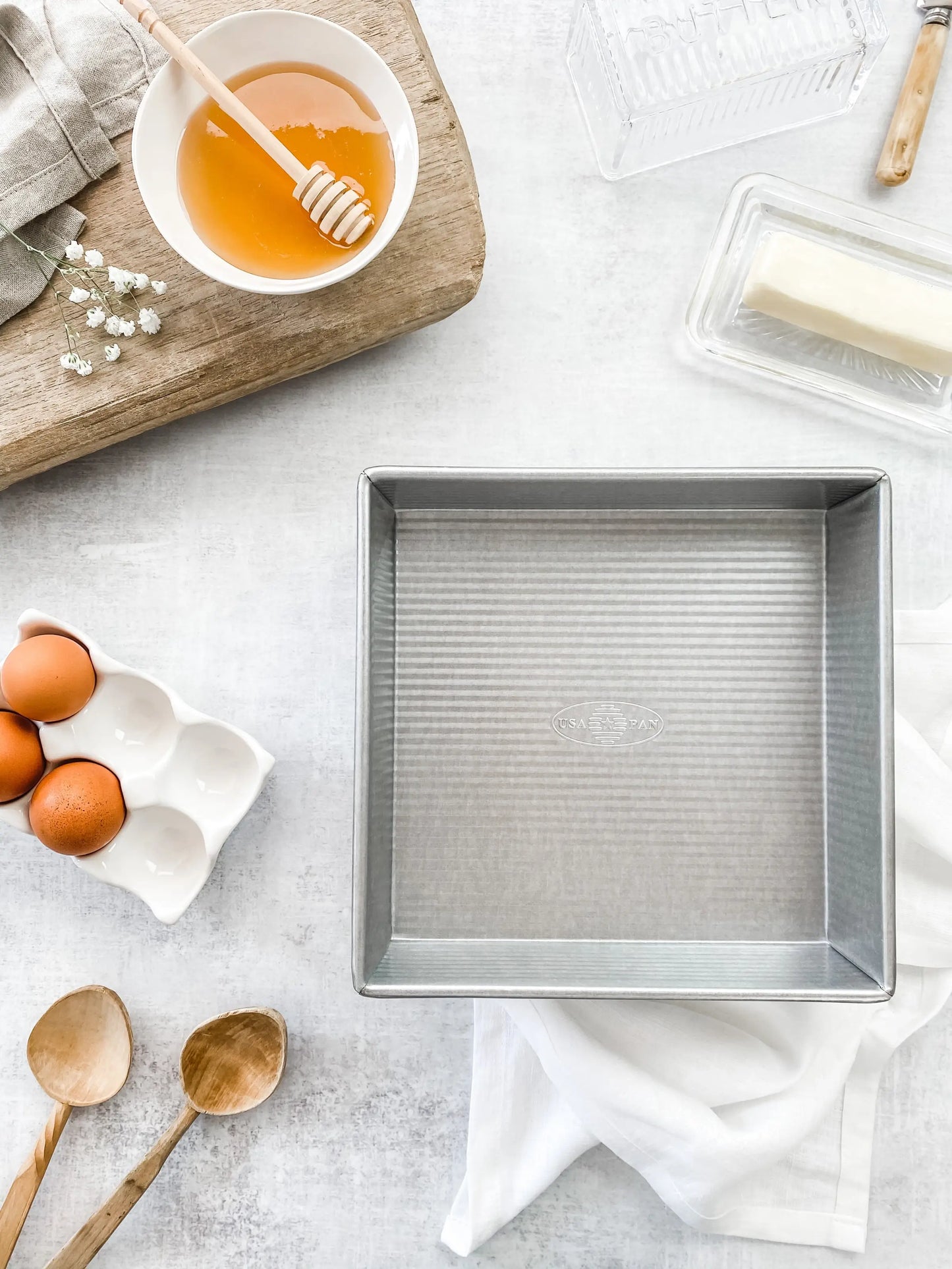 9 Inch Square cake pan on a white background with various baking items surroundind